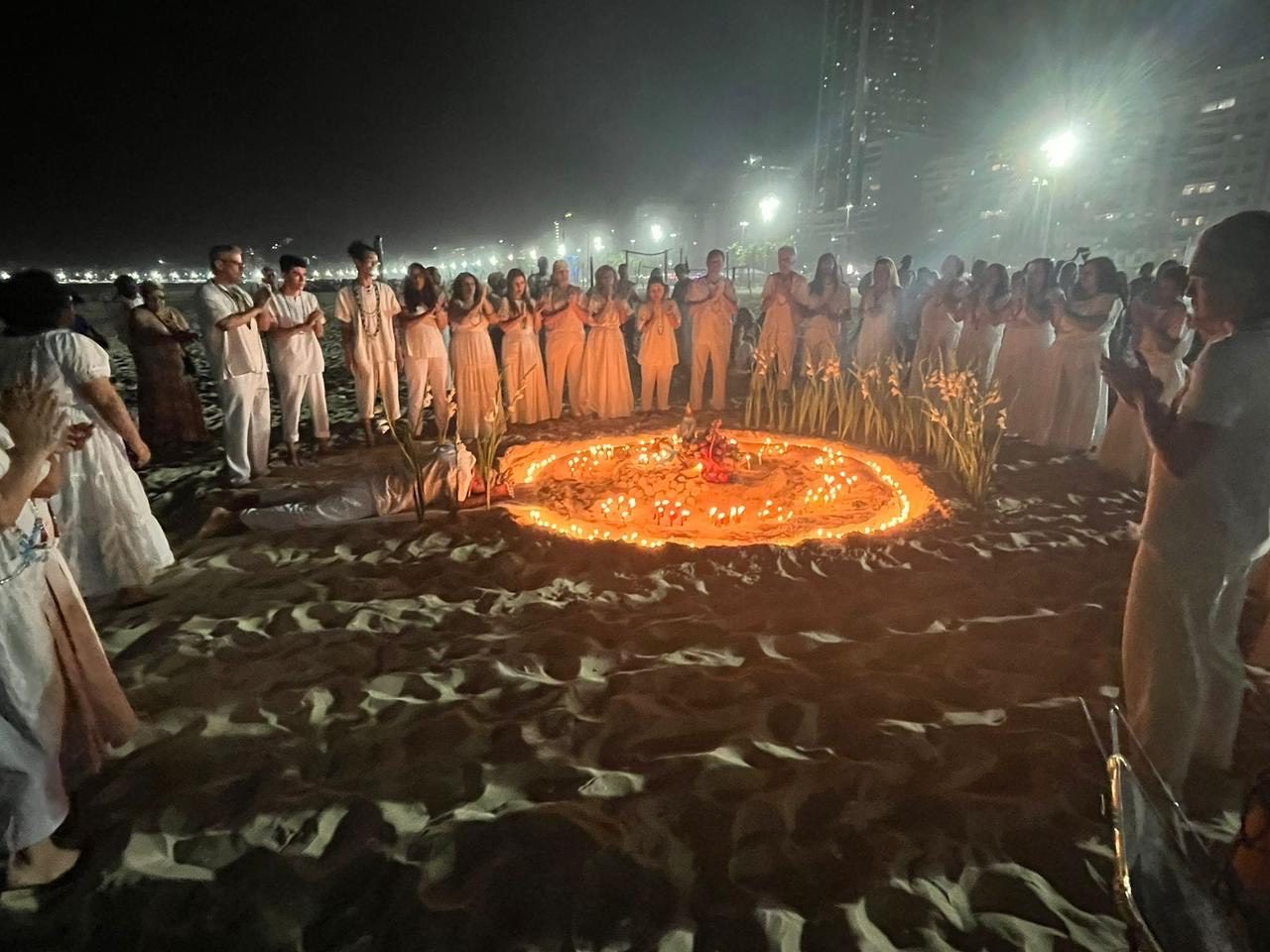 Roda de umbandistas em volta de um ponto de fogo na areia, à noite, na praia